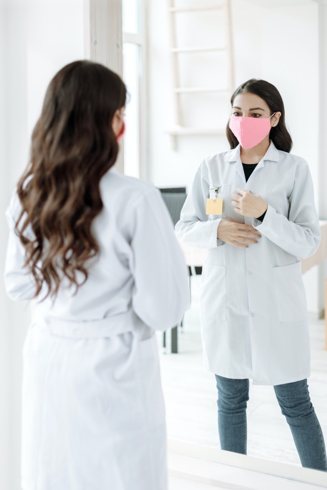 a person stands in front of a mirror dressed with a labcoat and a facemask