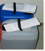 Photo of a large white container and a large blue container for collection of liquid chemical waste