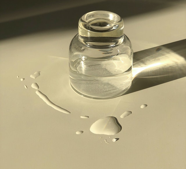 photo of a small glass jar with liquid and liquid spillage on the surface around it